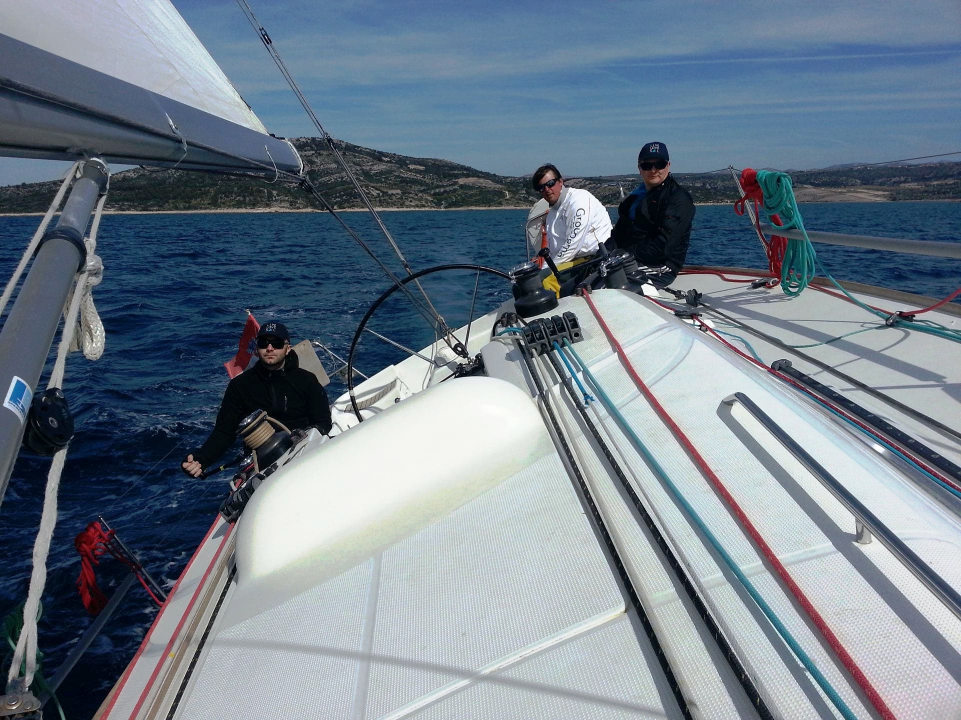 Three men handling a boat and sailing with hills in the distance