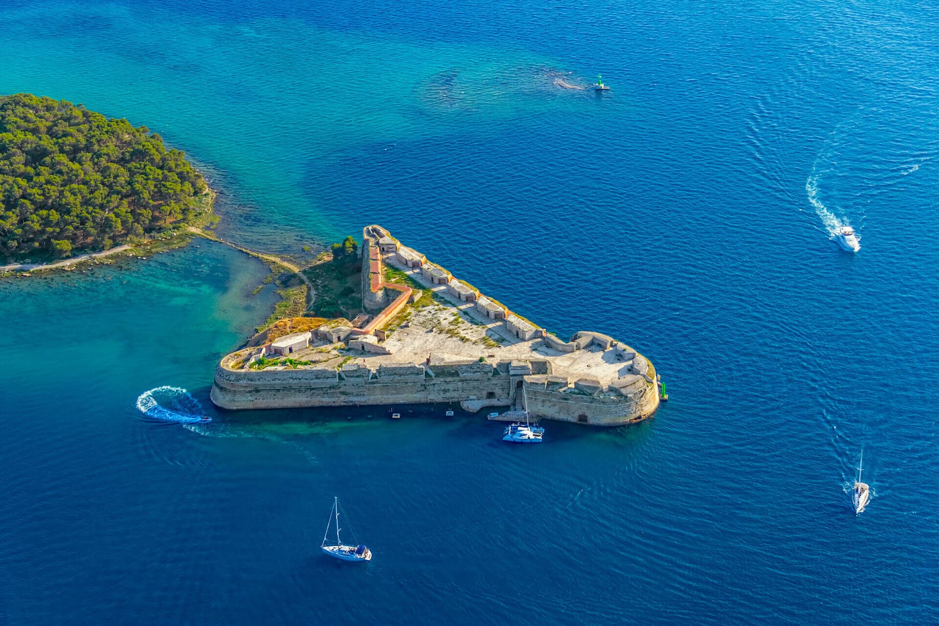 Yachts sailing and cruising around triangle shaped fort in the middle of sea