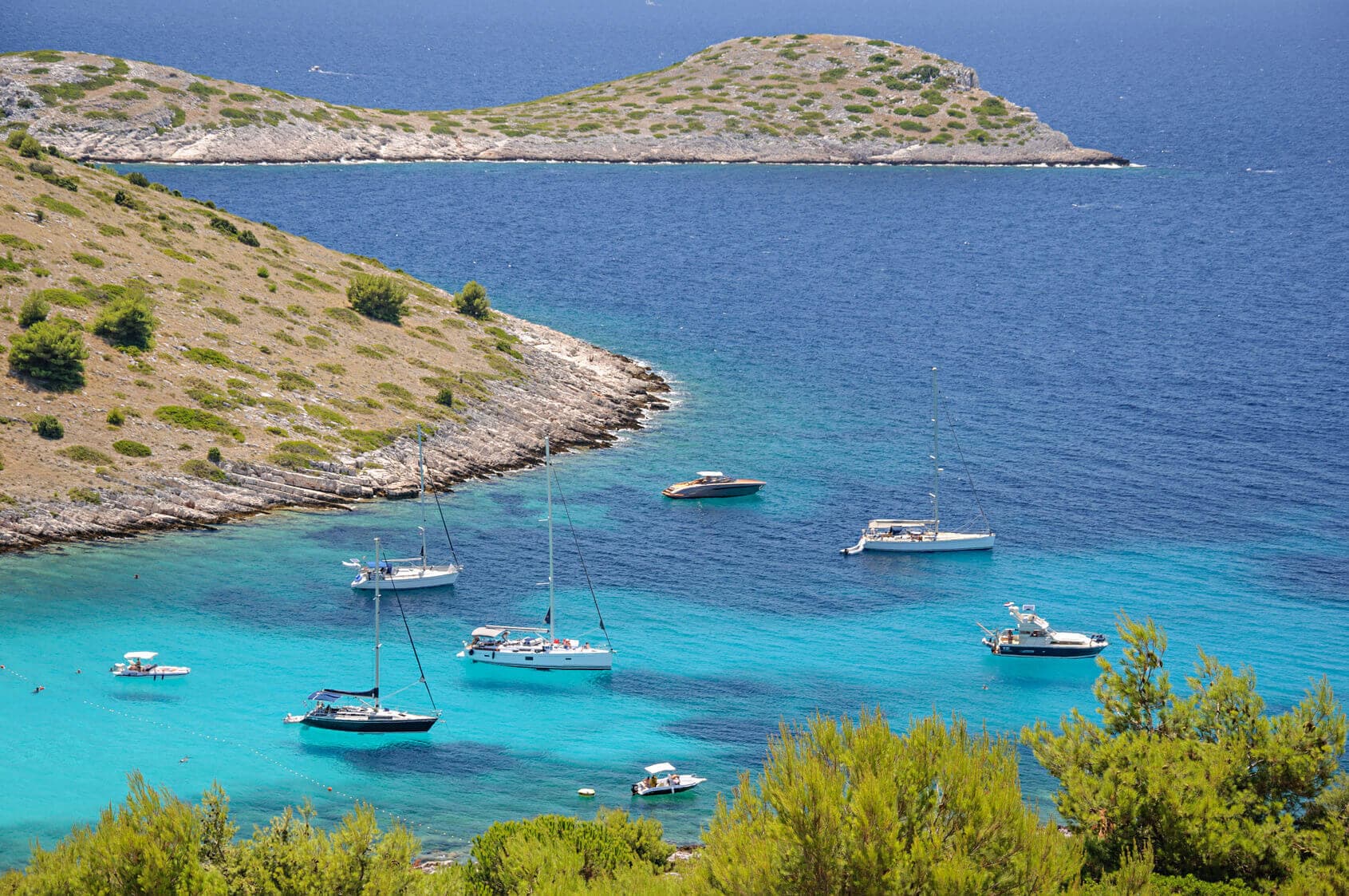 Aerial shot of yachst sailing on bright blue water with island in the background