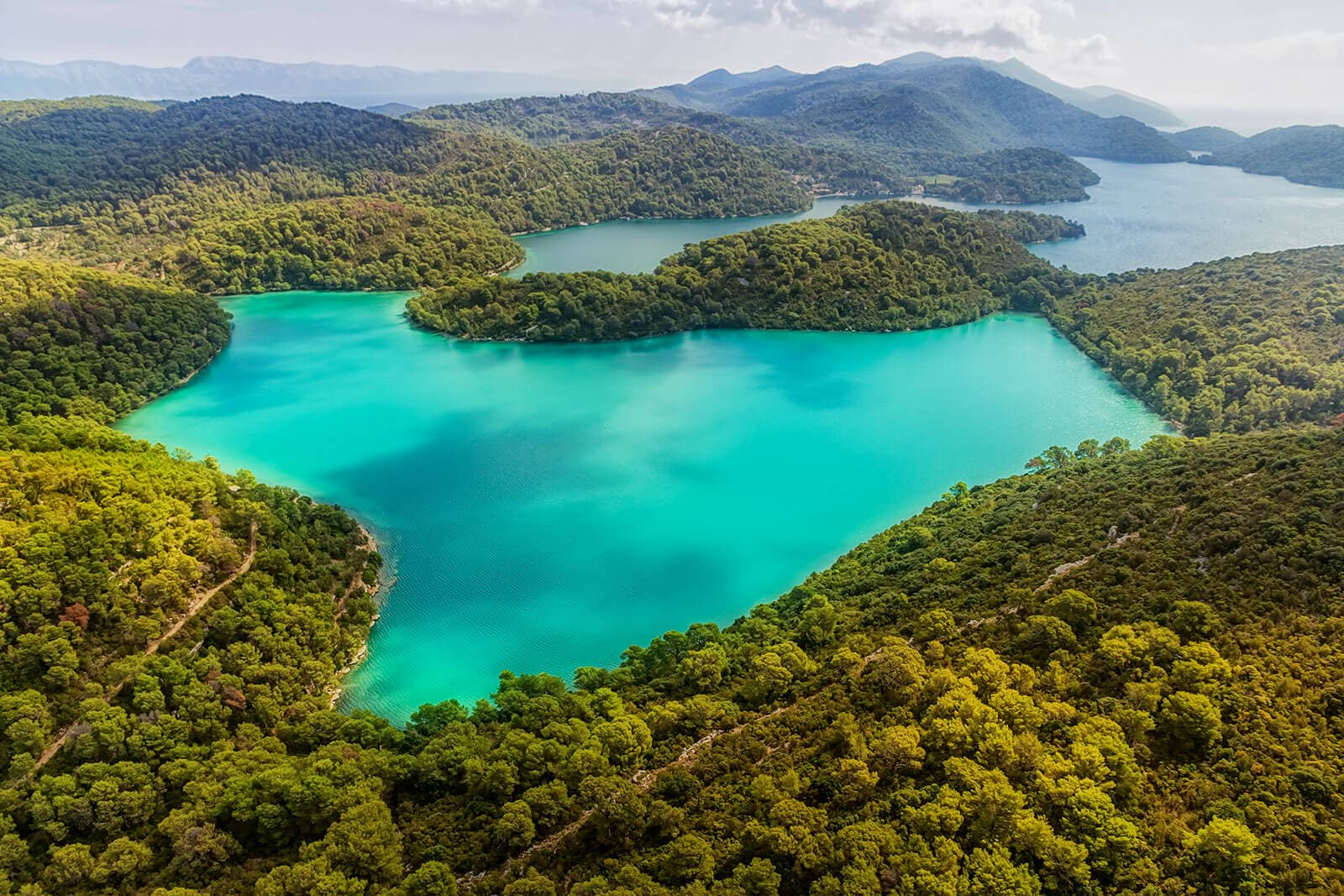 Turquiose water surrounded by greenery and hills in the distance