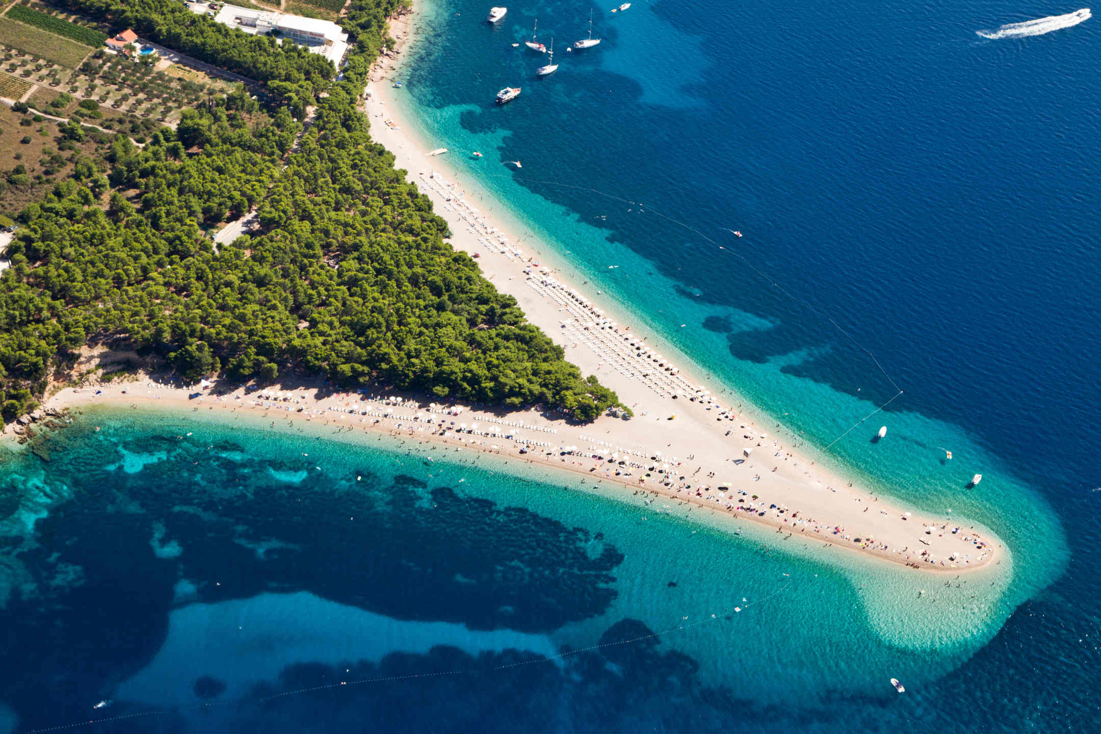 Triangle shaped beach with many tourists on it, surrounded by deep blue water